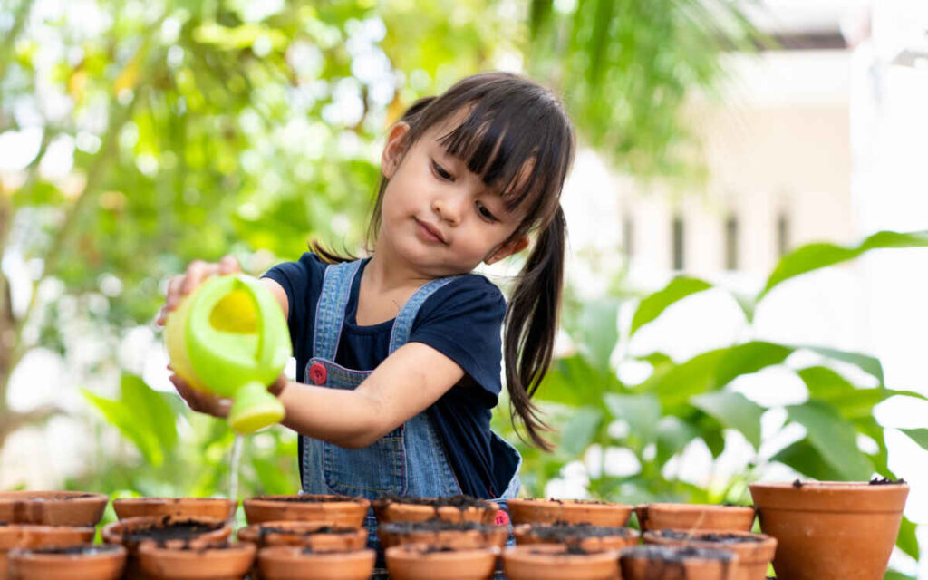 adorable 3 years old asian little girl is watering the plant in the pots outside the house, concept of plant growing learning activity for preschool kid and child education for the tree in nature