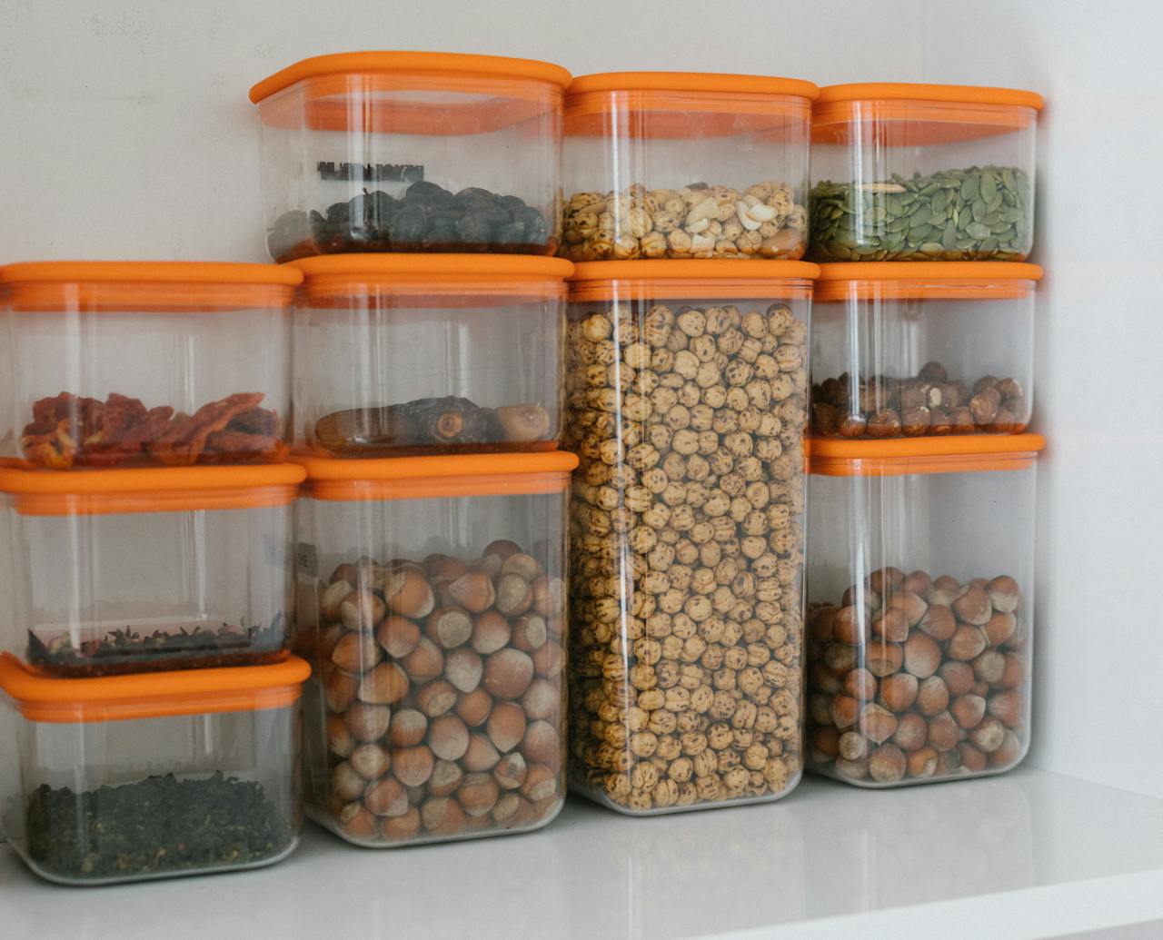 Various nuts and grains stored in transparent plastic containers with orange lids, organized neatly.